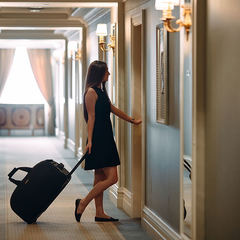 Young woman with handbag and suitcase in an elegant suit walks the hotel corridor to her room